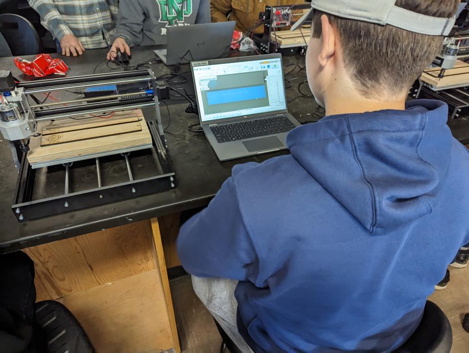 Student sitting at a computer near a CNC machine